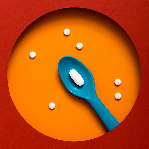 Top view of colored plastic spoon with pill