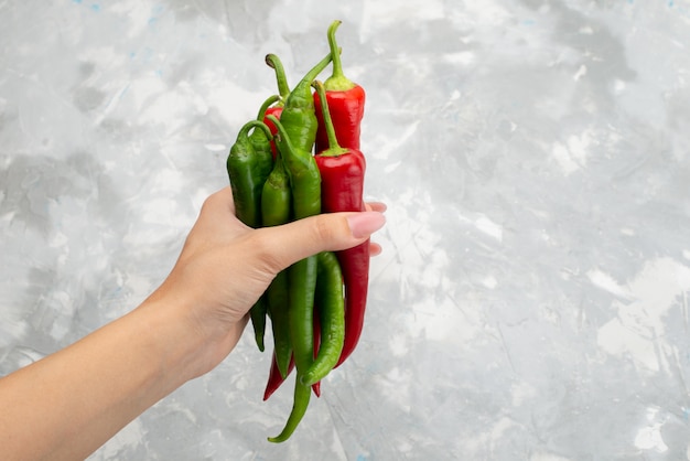 Free photo top view colored spicy peppers holding by female green and red on grey