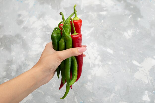 Top view colored spicy peppers holding by female green and red on grey