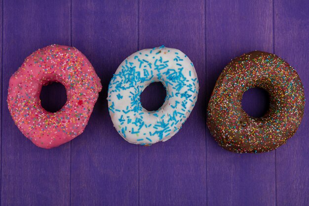 Top view of colored sweet donuts on a bright purple surface