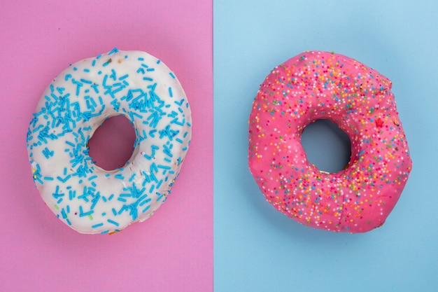 Top view of colored sweet donuts on a light blue-pink surface
