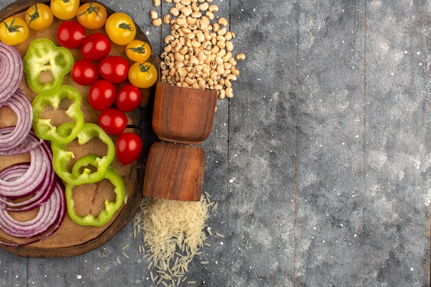 top view colored vegetables sliced onions green bell pepper and tomatoes on the brown desk and grey