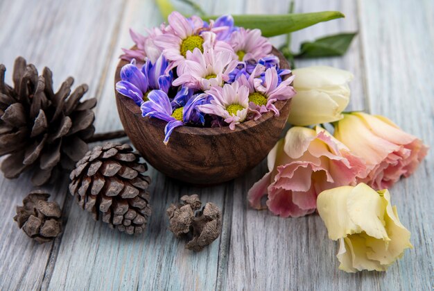 灰色の木製の背景に松ぼっくりと木製のボウルにカラフルな素晴らしいデイジーの花の上面図