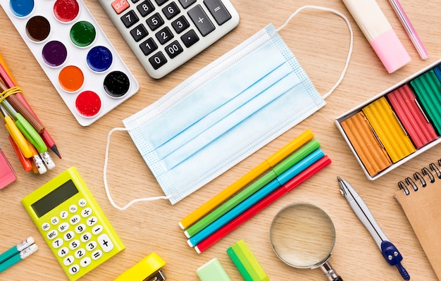 Top view of colorful back to school supplies with medical mask