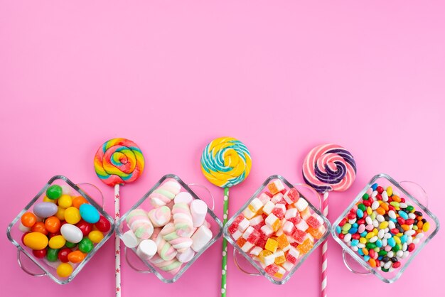 A top view colorful candies along with lollipops on pink desk