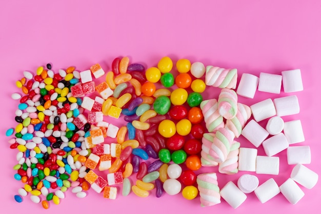ピンクの机の上の異なる色の甘くておいしいお菓子の平面図カラフルなキャンディー組成