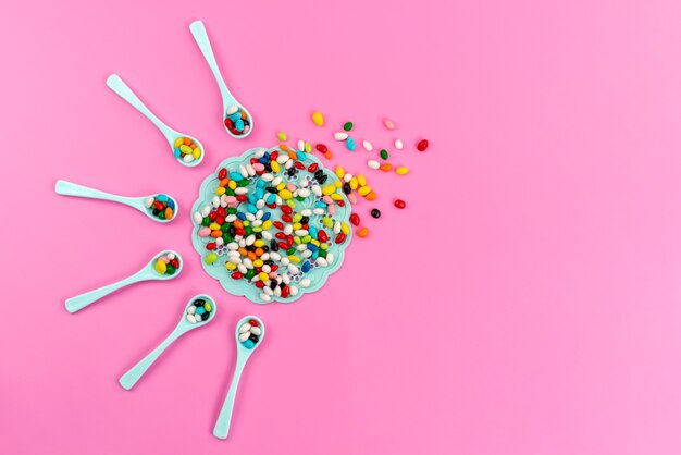 A top view colorful candies inside green spoons on pink