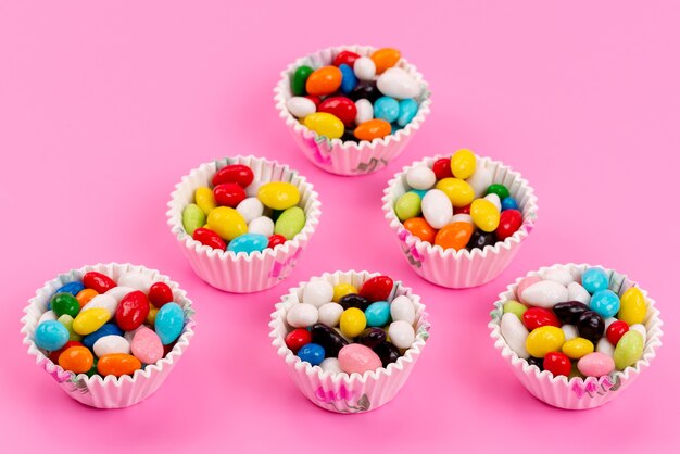 A top view colorful candies inside paper packages on pink