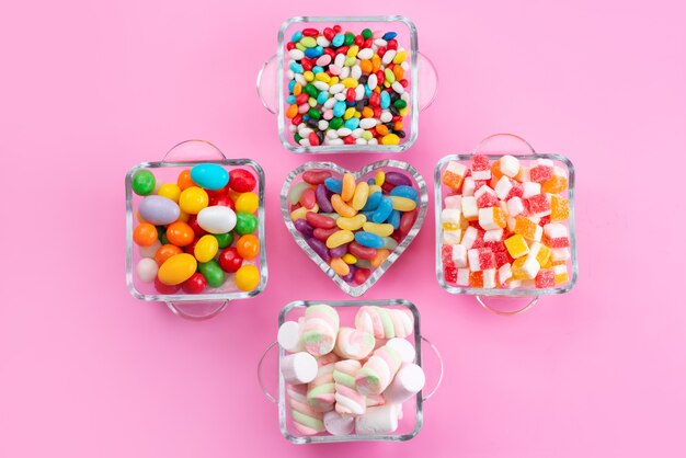Вид сверху красочные конфеты и зефир в очках на розовом столе, цветной сладкий сахар