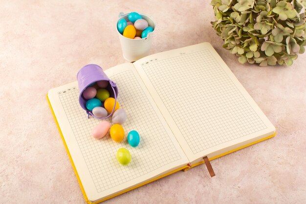 A top view colorful candies with copybook on the pink desk color sweet sugar goodie