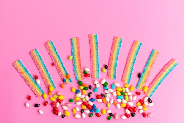 A top view colorful candies with rainbow marmalades on pink desk, sweet sugar rainbow