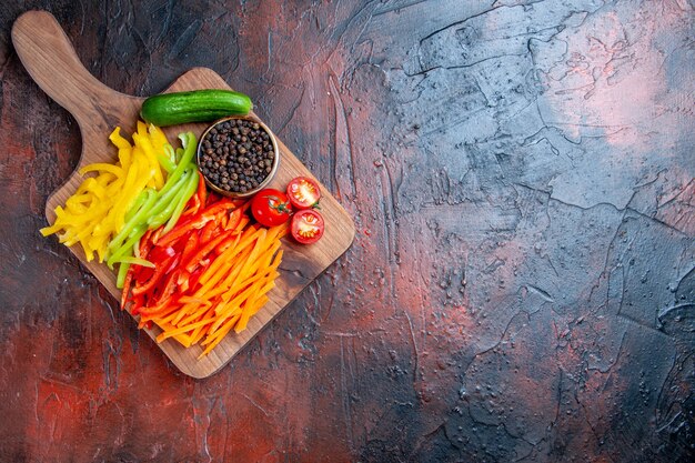 Top view colorful cut peppers black pepper tomatoes cucumber on chopping board on dark red table free space