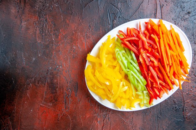 Top view colorful cut peppers on white plate on dark red table copy place