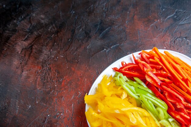 Free photo top view colorful cut peppers on white plate on dark red table with copy space