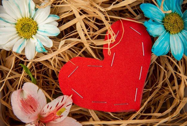 Top view of colorful daisy flowers and pink alstroemeria with a heart made from red color paper on straw table