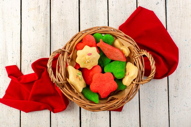 A top view colorful delicious cookies different formed inside brown basket on the grey surface