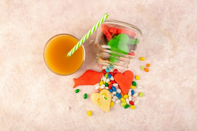 Top view of colorful delicious cookies different formed inside can with candies and fresh peach juice on the pink surface