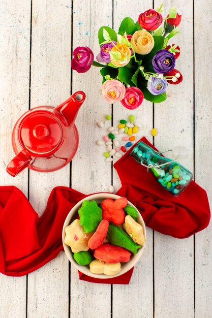 赤いやかんのお菓子と花のプレートの内側に形成された異なるカラフルなおいしいクッキーのトップビュー
