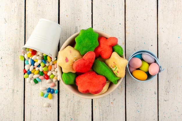 Top view of colorful delicious cookies different formed multicolored inside plate with candies on the grey surface