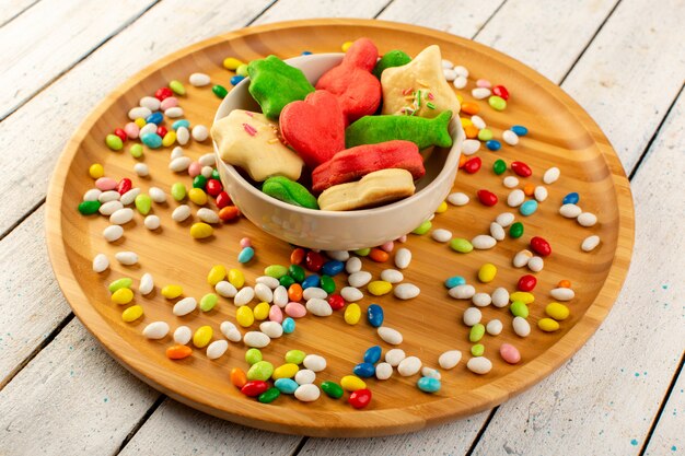 Top view of colorful delicious cookies different formed multicolored inside plate with candies on the wooden desk