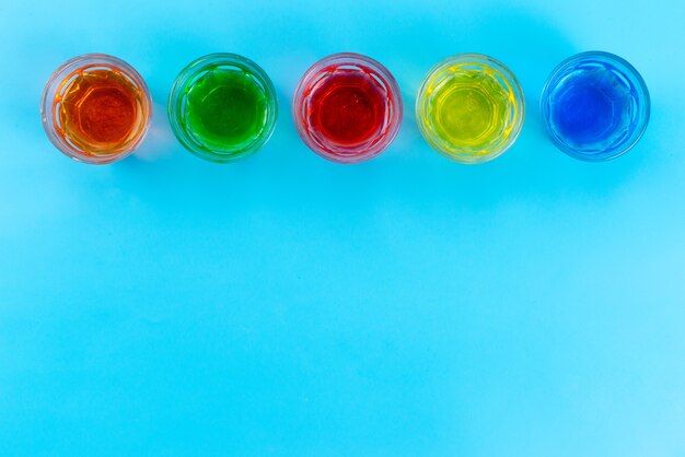 A top view colorful drinks inside transparent glasses on blue, drink juice fruit color