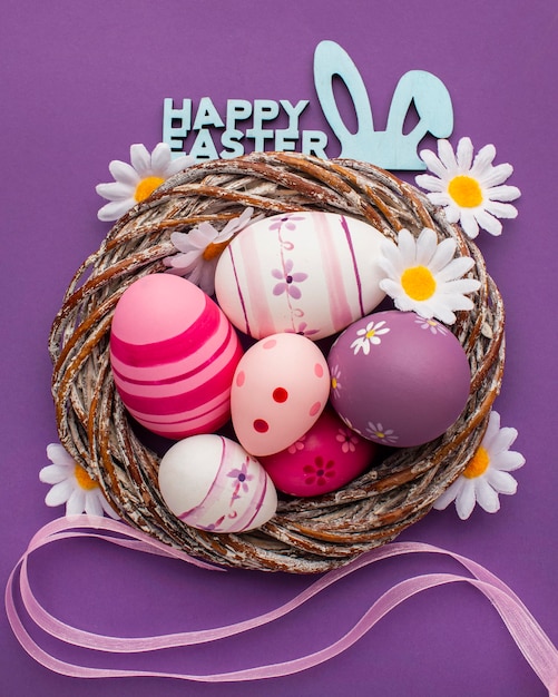 Top view of colorful easter eggs in basket with chamomile flowers