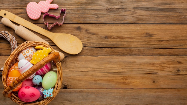 Top view of colorful easter eggs in basket with kitchen utensils and copy space