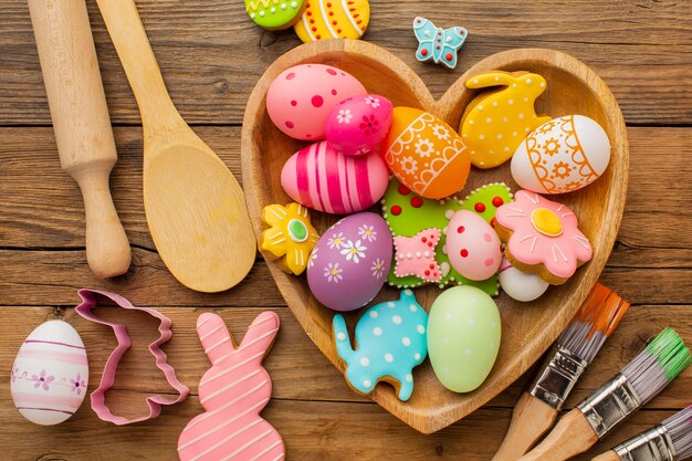 Top view of colorful easter eggs in heart shaped plate with kitchen utensils and paint brushes