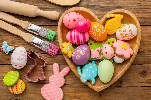 Top view of colorful easter eggs in heart shaped plate with kitchen utensils