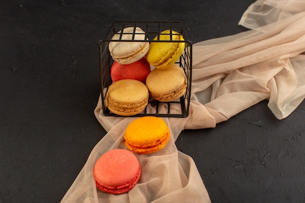 A top view colorful french macarons delicious and baked inside basket on the dark table cake biscuit cookie sugar