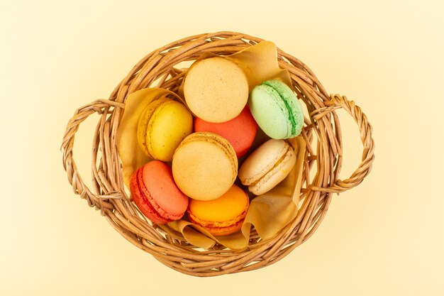 A top view colorful french macarons inside basket on the yellow desk cake biscuit sugar sweet