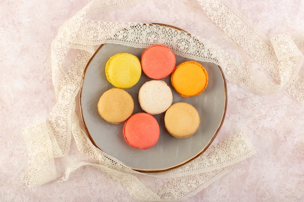 Una vista dall'alto macarons francesi colorati all'interno del piatto rotondo sul colore rosa dello zucchero del biscotto della torta dello scrittorio