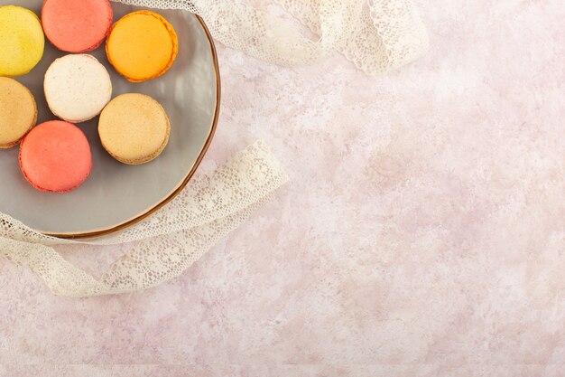 A top view colorful french macarons yummy inside plate on the pink desk cake biscuit sugar sweet