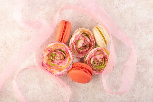 A top view colorful french macarons yummy with flowers on the pink desk sugar cake biscuit