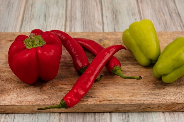 Top view of colorful fresh bell and chili peppers on a wooden kitchen board on a grey wooden background