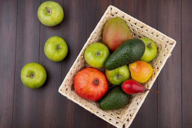 Top view of colorful fruits such as apple pear mango on bucket with green apples on wood