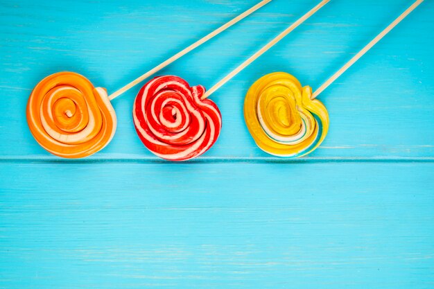 Top view of colorful lollipops on a stick on blue wooden background with copy space