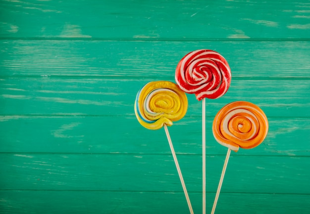 Free photo top view of colorful lollipops on a stick on green wooden background with copy space