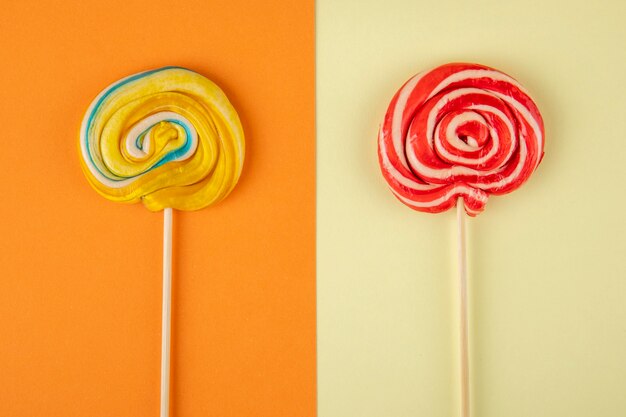 Top view of colorful lollipops on a stick on orange and cream background