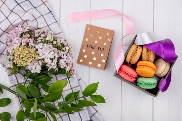 색깔의 상자에 다채로운 마카롱의 상위 뷰 흰색 표면에 꽃의 꽃다발과 엽서를 활