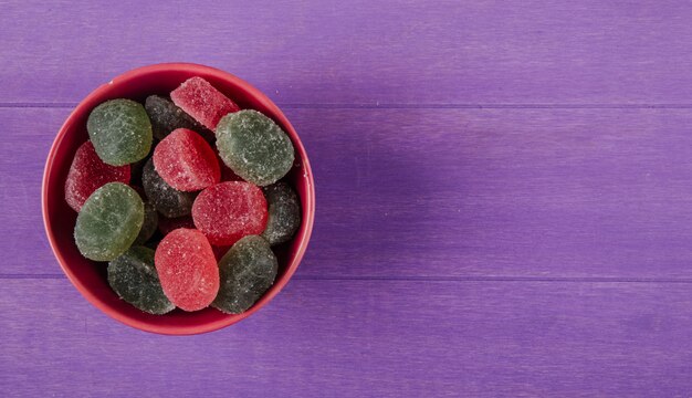 Вид сверху красочные мармеладные конфеты в миску на фиолетовом фоне деревянных