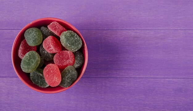 Top view of colorful marmalade candies in a bowl on purple wooden background