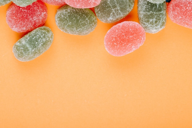 Top view of colorful marmalade candies scattered on orange background with copy space