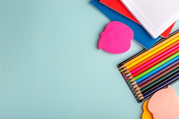 Foto gratuita vista dall'alto matite colorate con quaderni sulla parete blu penna colore scuola bambini bambini