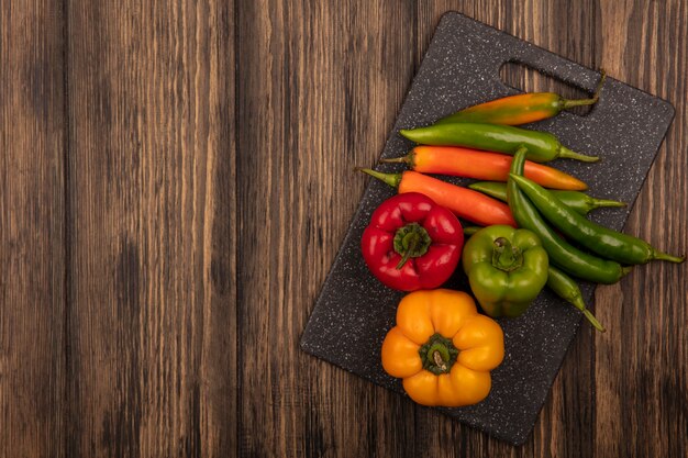 Top view of colorful peppers on a black kitchen board on a wooden background with copy space