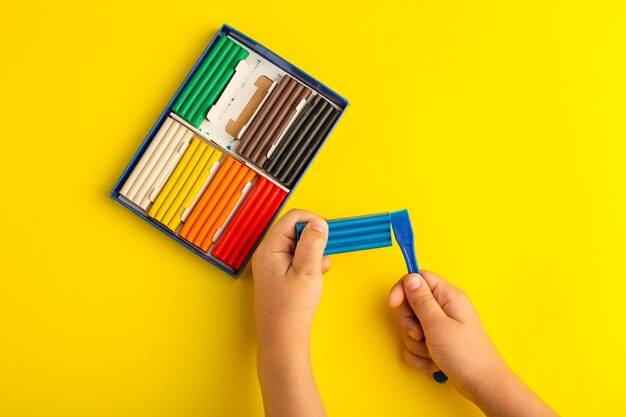 Top view colorful plasticines child working and playing with it on yellow wall color photo kid school