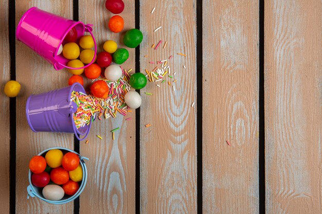 Вид сверху разноцветных брызг и конфет, разбросанных из маленьких ведер
