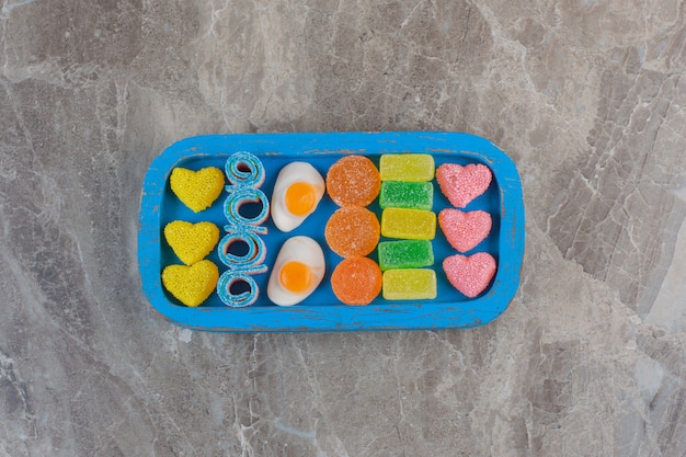 Top view of colorful sweet candies on blue wooden plate.