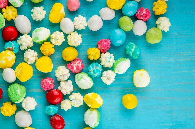 Top view of colorful sweet sugar candies scattered on blue wooden background