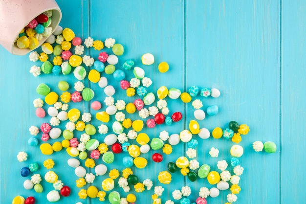 Free photo top view of colorful sweet sugar candies scattered from a bowl on blue wooden background